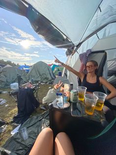 a woman sitting at a table in front of a tent with beer and food on it