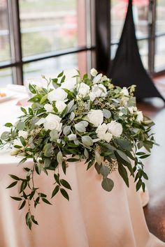 white flowers and greenery sit on a table in front of large windows at a wedding reception