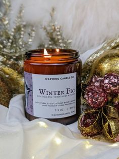 a candle sitting on top of a white blanket next to christmas decorations and ornaments in gold foil