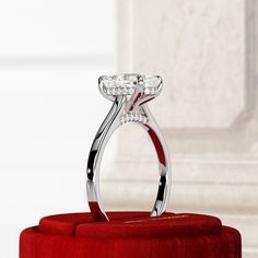 a diamond ring sitting on top of a red velvet cushion in front of a white wall