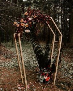 a wooden arch decorated with flowers and greenery stands in the middle of a forest