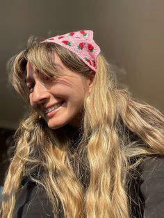 a woman with long blonde hair wearing a pink knitted strawberry headband and smiling