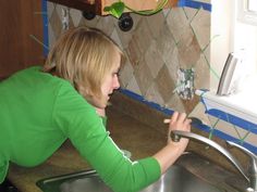 a woman in green shirt fixing a sink faucet on the side of a kitchen counter