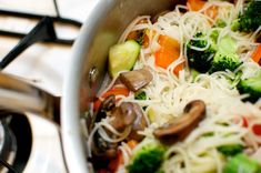 broccoli, carrots, and noodles are being cooked in a pan on the stove