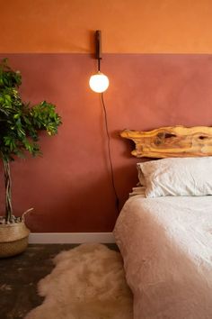 a bed with white sheets and pillows next to a potted plant on the wall