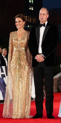 two people standing on a red carpet next to each other wearing evening gowns and tuxedos