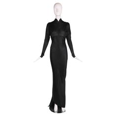 1986 F/W Azzedine Alaia black acetate knit floor-length evening gown with stand collar, vertical gathers at the bust that create a unique shoulder detail and an open back in the shape of a deep V to the waistline. The fabric is cut on the bias and punctuated with diagonal seaming from front to back which forms an asymmetric train at the hem. There is a built-in body suit at the interior with a snap closure. Size tag M, 100% acetate. In excellent condition. Please consult measurements. Shoulders: Fitted Black Gown With Bias Cut, Evening Gown With Long Train, Fitted Bias Cut Maxi Dress For Dinner, Fitted Maxi Dress With Sweep Train For Evening, Evening Bias Cut Full Length Gown, Evening Gown With Bias Cut Full Length, Evening Gown With Bias Cut In Full Length, Fitted Floor-length Gown For Dinner, Fitted Floor-length Dinner Gown