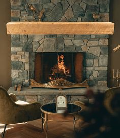 a stone fireplace in a living room with two chairs and a table next to it