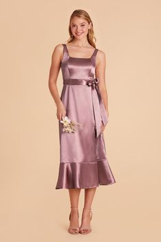 a woman wearing a purple dress with a flower on the side and a bow at the waist