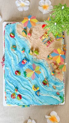 there is a cake decorated with umbrellas and people on the beach in the sand