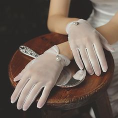 a woman wearing white gloves sitting on top of a wooden table next to a mirror