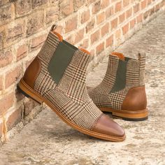 a pair of brown and green boots next to a brick wall