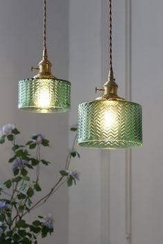 two green lamps hanging from a ceiling next to a vase with blue flowers in it