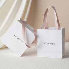 two white paper bags with pink ribbons on them