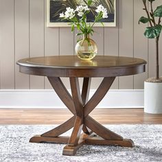 a round wooden table sitting on top of a carpeted floor next to a potted plant