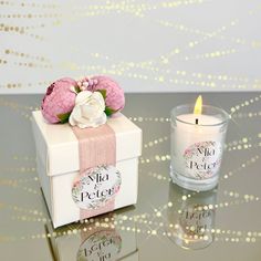 a small white box sitting on top of a table next to a pink flower and candle