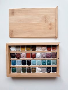 an open wooden box filled with lots of different colored scarves on top of a white wall