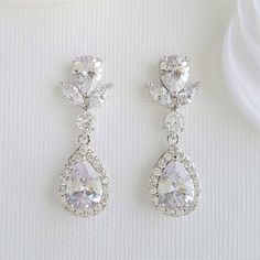 two pairs of diamond earrings sitting on top of a white cloth