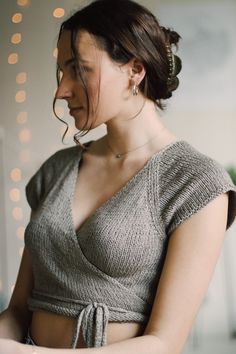 a woman in a gray top is holding a cell phone and looking down at her wrist