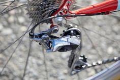 the rear wheel of a bicycle with red brake pads and blue rims on gravel ground