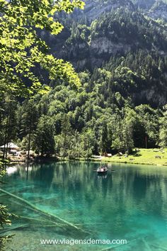 a lake surrounded by mountains and trees with clear water in the foreground, on a sunny day