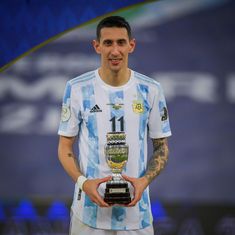 a male soccer player holding a trophy and smiling at the camera while standing in front of a large screen