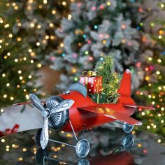 a red toy airplane with presents on it sitting in front of a decorated christmas tree