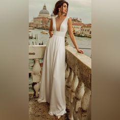 a woman in a white dress standing on a bridge next to the water and looking off into the distance