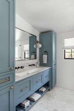 a large bathroom with blue cabinets and marble counter tops, along with white tile flooring