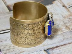 This bracelet is a brass metal cuff with a repurposed vintage repurposed brooch glued on top. A great gift for the vintage lover in your life. IT E M ∙ S P E C I F I C A T I O N S: - CUFF: Metal cuff is brass with a engraved floral detail and measures 6" X 1 1/2" - EMBELLISHMENT: Blue and clear rhinestone brooch is prong set and measures 1 1/2" x 1 1/8" C A R E ∙ T I P S: We don’t want your special moment to fade. To maintain the quality of your jewelry, please: - Do not wear it to the pool, spa Vintage Nickel Free Cuff Jewelry, Nickel-free Vintage Cuff Jewelry, Vintage Nickel-free Cuff Jewelry, Antique Finish Bracelet For Gift, Unique Antique Finish Bracelet As Gift, Costume Jewelry Cuff Bangle Bracelet For Gift, Vintage Brass Cuff Bracelet For Formal Occasions, Vintage Antique Gold Brass Cuff Bracelet, Vintage Gold Cuff Bracelet With Antique Finish