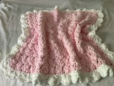 a pink and white crocheted blanket laying on top of a bed