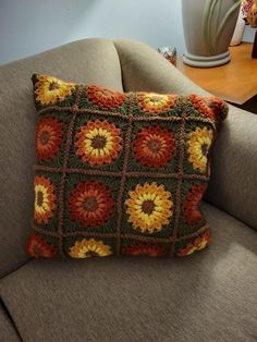 a crocheted pillow sitting on top of a couch next to a vase with flowers