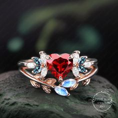 a red heart shaped ring with leaves and stones on top of a green leafy rock