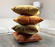 four pillows stacked on top of each other in front of a white couch and table