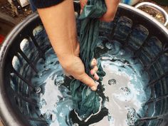 a person is washing their hands in a large metal bucket filled with blue and green liquid