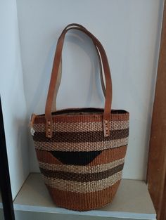 Geometrical earth tone sisal tote bag. Unique and stylish colorful sisal kiondo bag with stitched leather straps, pocket lining and zipper. Patterns and sizes slightly vary because weaving and stiching is done by hand. Ideal as a beach bag, shopping basket, market basket or storage basket. This unique tote bag is handmade by a group of ladies in a remote rural village in Machakos, Kenya. Do not clean with brush or water. If the bag gets wet, please dry to avoid dampness.  Leather type used is bo Natural Straw Satchel Bag With Removable Pouch, Natural Straw Satchel With Removable Pouch, Brown Woven Bucket Bag Shaped As Tote, Brown Woven Tote Bucket Bag, Eco-friendly Brown Bag With Braided Handles, Brown Bucket Shoulder Bag With Handles, Natural Handheld Satchel With Removable Pouch, Modern Bags With Leather Handles For Market, Eco-friendly Woven Brown Bucket Bag