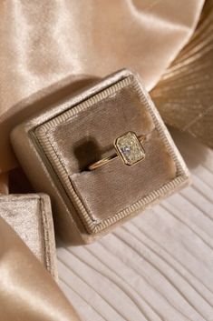 an engagement ring in a velvet box on a satin fabric background with gold cloths