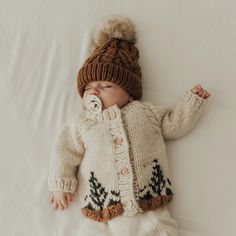 a baby wearing a knitted sweater and hat laying on top of a white sheet