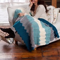 a woman is sitting on a couch with a crocheted blanket