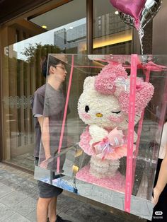 a man standing next to a giant teddy bear in a box with pink ribbon on it