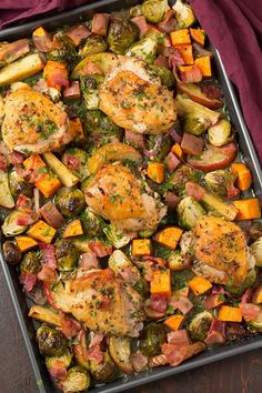 a pan filled with chicken and vegetables on top of a red table cloth next to a fork