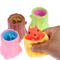 a hand holding a toy animal in front of three plastic vases with different colors