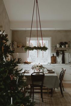 a dining room table with christmas decorations hanging from it's ceiling and candles on the windowsill