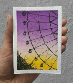 a hand holding up a purple and yellow card with an image of a ferris wheel