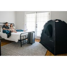 a man and woman sitting on a bed in a bedroom with a tent next to them