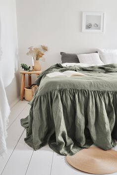 the bed is made with green linens and has a round wooden floor mat in front of it