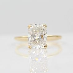 a yellow gold engagement ring with a cushion cut diamond in the center, on a white surface