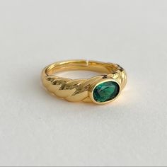 a close up of a gold ring with a green stone in the center on a white surface