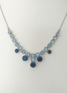 "This shimmering 1950s necklace features sparkling, faceted sapphire-blue and diamond-white crystals. A silver tone curb chain links each side of the pendant to a spring ring clasp.  The diamante element is 9 cm x 1.5 cm (about 3.5\" x 0.6\"), and the overall length is 43 cm (17\"). Patina on metal elements is commiserate with age; see photos. This 50+ year old necklace is in lovely, wearable vintage condition, and is perfect for formal occasions, weddings, proms and more. Please note: * Cream-coloured \"pearls for a princess\" display case in photos is for styling purposes only, and is not included. * Crystals/gemstones and metal elements of jewellery may feature aged patina. Additional: * As I am a resale shop, all my items are in vintage or antique preloved condition and as seen. Please 1950s Necklace, Prom Necklace, Old Necklace, Vintage Rhinestone Necklace, Prom Necklaces, White Crystals, Chain Links, Necklace Blue, Vintage Pearls