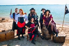 a group of people dressed in pirate costumes posing for a photo on the beach with an old barrel